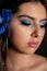 Close up charming, mysterious, romantic brunette woman with blue makeup and blue orchid flowers in hair. Skin, body care