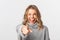 Close-up of cheerful attractive blond girl, pointing at camera and smiling, choosing you, standing over white background