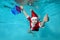 Close-up of a cheerful little boy in a Santa Claus costume underwater. He dives to the bottom of the pool with a new