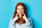 Close-up of cheerful teenage girl with red hair and freckles, poking cheeks, showing dimples and smiling with white