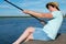 Close-up, cheerful woman in a hat on a pier, holds a fishing pole and pulls out a fish catch, on the background of a beautiful