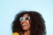 Close up cheerful young african woman in sunglasses looking away and laughing on blue background