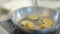 Close up of chef cooker in black gloves friyng or stewing slices of zucchini and corn on a hot pan with oil.