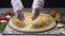 Close-up of chef`s hands covering the pizza dough with cheddar on a wooden board before the other ingredients. Frame