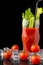 Close-up of cherry tomatoes with ice, bloody mary cocktail with celery and black straw, with selective focus, on wet slate and bla