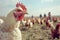 Close-up chicken looking in the camera with a group of people in a field.