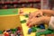 Close up of child`s hands playing with colorful plastic bricks at the table. Early learning. stripe background. Developing toys