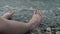 A close-up of a child`s legs is overwhelmed by a wave. Pebble sea beach noisy sea waves on children`s legs