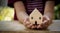 Close up of children`s hand holding wooden house on wooden table, hope for new house, thinking for home