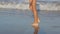 Close-up of children`s legs of a girl walking on the beach. Walk around the sea. A look at the sea waves that come to
