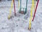 Close up of children's swing in early spring. Wet swing on playground in slushy weather with melted snow.