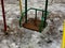 Close up of children's swing in early spring. Wet swing on playground in slushy weather with melted snow.