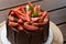 Close up of chocolate cake covered with strawberries, basil leaves, blackberry jam and with chocolate plates around it.