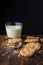 Close-up of chocolate chip cookies, crumbs, spoon and glass of milk, with selective focus, on wooden table and black background