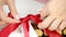 Close-up chocolatier ties red bow on gift box of chocolate candies, slow mo