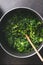 Close up of chopped stewed spinach in cooking pan with wooden spoon on rustic kitchen table. Top view. Vegetarian healthy eating