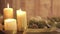 Close up of a Christmas setting with moving flames of a lit candle, pine boughs, natural pine cones, red baubles, golden satin and