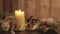 Close up of a Christmas setting with moving flames of a lit candle, pine boughs, natural pine cones, red baubles, golden satin and