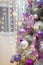 Close up of Christmas tree branches with purple decorative baubles and bokeh lights on background. New Year garlands.