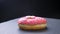 Close-up circling around shot of delicious glazed pink donut with multicolored chips and eyes spinning slowly on gray