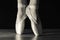 Close-up classic ballerina`s legs in pointes on the black background and wooden grey floor.