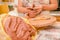 Close up of a clay mass with a blurred woman ceramist behind working on sculpture on wooden table in workshop, in a