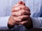 Close up or closeup of hands of faithful mature man praying. Hands folded, interlaced fingers in worship to