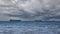 Close-up of a cloudy seascape on a rainy summer day. Blue sea, storm clouds over the horizon, and several cargo ships