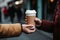 A close-up of a coffee cup passing between hands, capturing a shared moment in a bustling urban setting