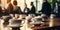 Close-up of coffee cups on a conference room table with blurred business professionals engaging in discussions in a bright