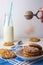 Close-up of colander with chocolate powder falling on white plate with chocolate chip cookies, spoon, bottle of milk, with selecti
