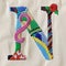 A close up of a colorful embroidered letter n, embroidery on white background