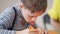 Close-up concentrated autistic Caucasian boy painting with tongue out sitting at table indoors. Focused child with