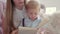 Close-up of concentrated toddler looking into book as unrecognizable mother reading story. Portrait of cute little