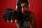 Close-up of concentrated young African athletic woman boxer in headphones and red boxing gloves making a straight kick, 