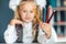 Close-up concept of colored pencils in the hands of a blondy schoolgirl who keeps them at face level at the table. A schoolgirl