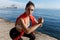 Close-up of confident fitness woman doing squats exercises near the sea, looking at camera during workout