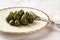 Close-up of conserved whole unripe figs and dessert fork on a white porcelain plate over marble surface. Traditional mediterranean