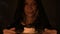 Close-up of a contented girl magician in a dark room by candlelight conjured herself a cake. Holds a plate of cake Low