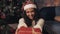 Close up of contented young girl wearing santas hat and white pullover, stretching out red gift box to camera smiling