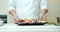 Close-up of cook`s hands in gloves serving a dish of fresh fish and vegetables on an ice substrate. Asian food