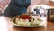 Close-up of cook serving mashed potatoes prepared with herbs in white plate.