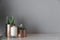 Close up copper vase with artificial plant inside and white candle in glass on cream spray-painted working table with gray pain