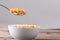 Close-up of cornflakes in spoon over breakfast bowl on table against gray background