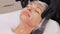 Close-up, cosmetologist in black medical gloves applies cosmetic gel emulsion to female face with massage movements