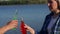 Close-up of a couple clink bottles of alcohol on the background of the lake.