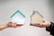 Close-up Of Couple\'s Hand Holding Different Miniature Houses