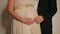 Close-up of a couple\'s hands on a pregnant tummy in a wedding dress.