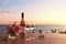 Close up of couple wine champagne glasses and bottle for celebration on wooden table with sea view and sunset sky background,