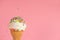 Close up of creative concept with ice cream cone and dynamic strewed sprinkles on pink background